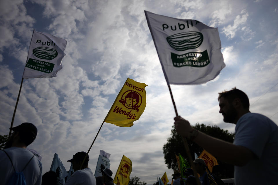 Farmworkers and allies hold flags calling out Publix and Wendy's as they prepare to begin a five-day trek aimed at highlighting the Fair Food Program, which has enlisted food retailers to use their clout with growers to ensure better working conditions and wages for farmworkers, Tuesday, March 14, 2023, in Pahokee, Fla. (AP Photo/Rebecca Blackwell)