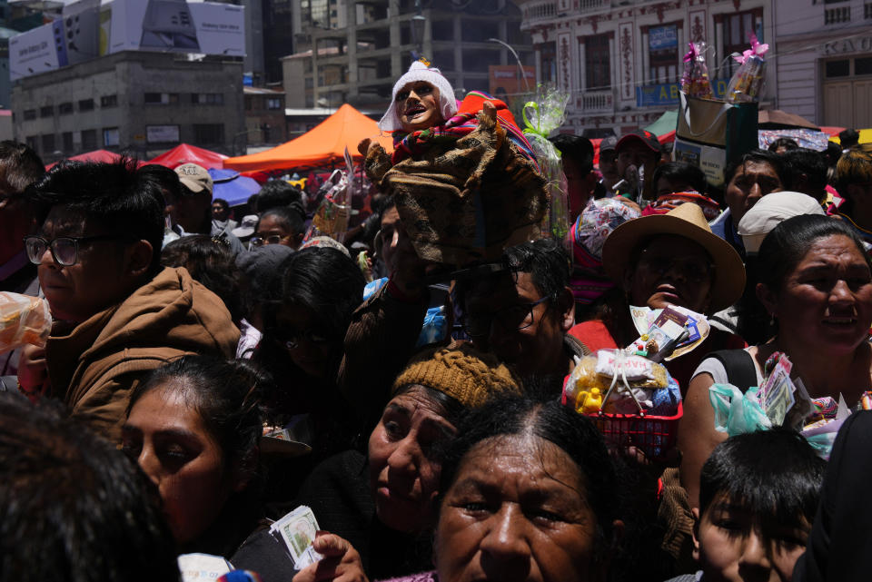 Un hombre lleva una figura en miniatura de Ekeko, dios de la abundancia, para que sea bendecido por un cura católico a las afueras de la iglesia de San Francisco durante la feria anual de Alasita en el centro de La Paz, Bolivia, el miércoles 24 de enero de 2024. En el día de inauguración de la feria se ofrecen réplicas en miniatura de las cosas que las personas anhelan o desean, como casas, vehículos o salud, para que se conviertan en realidad. Alasita es una palabra aymara que significa "cómprame". (AP Foto/Juan Karita)