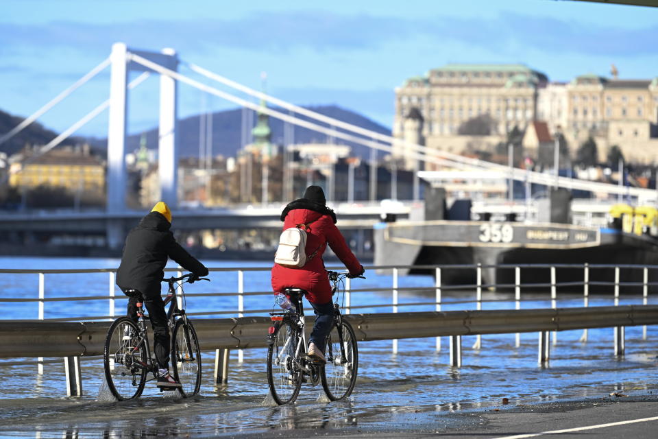 Two cyclists ride as the Sara Salkahazi quay is flooded by the river Danube at Fovam square in downtown Budapest, Hungary, Wednesday, Dec. 27, 2023. Due to the recent rains and snow, the water level of the Danube has risen. (Tamas Kovacs/MTI via AP)