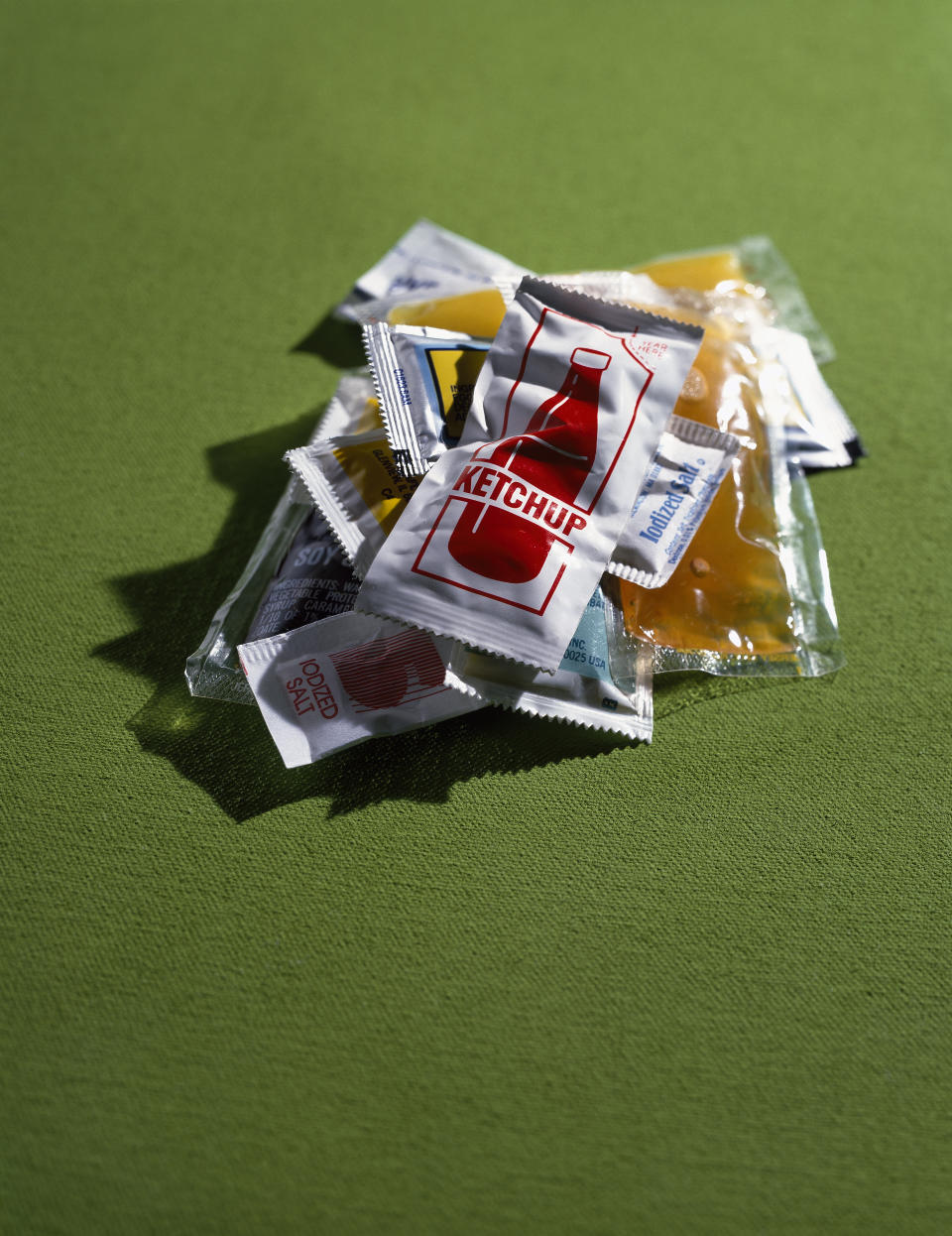 A variety of condiment packets, including ketchup, are scattered on a green surface