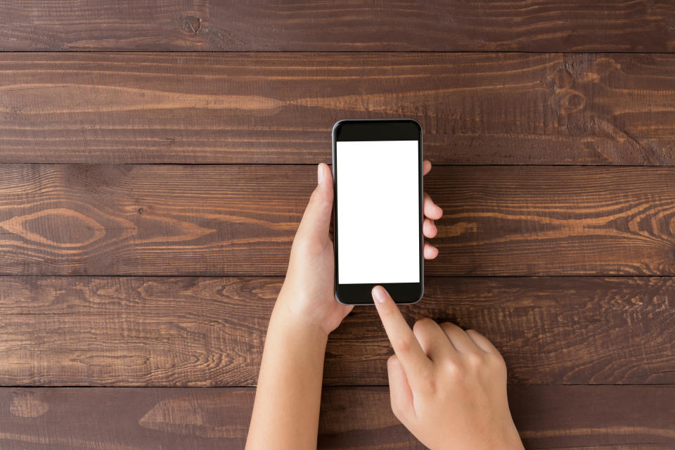 Hand holding a smartphone above a wooden surface