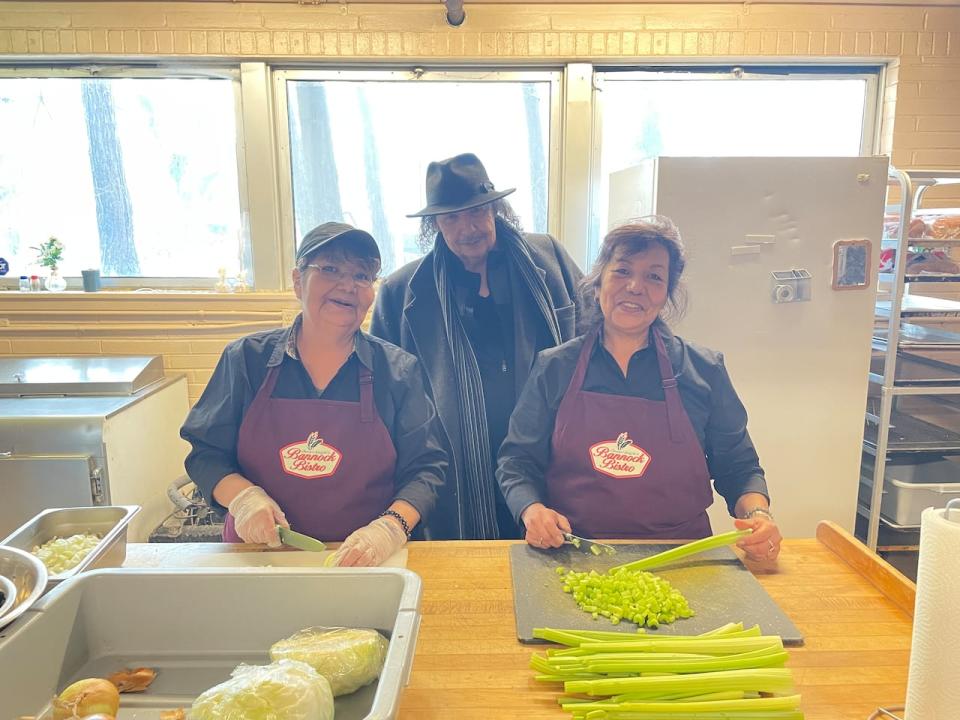 Chester Knight's Bannock Bistro head Chef Brenda Knight, and her sister Karen Pahtayken chop up vegetables while cree musician "supervises."