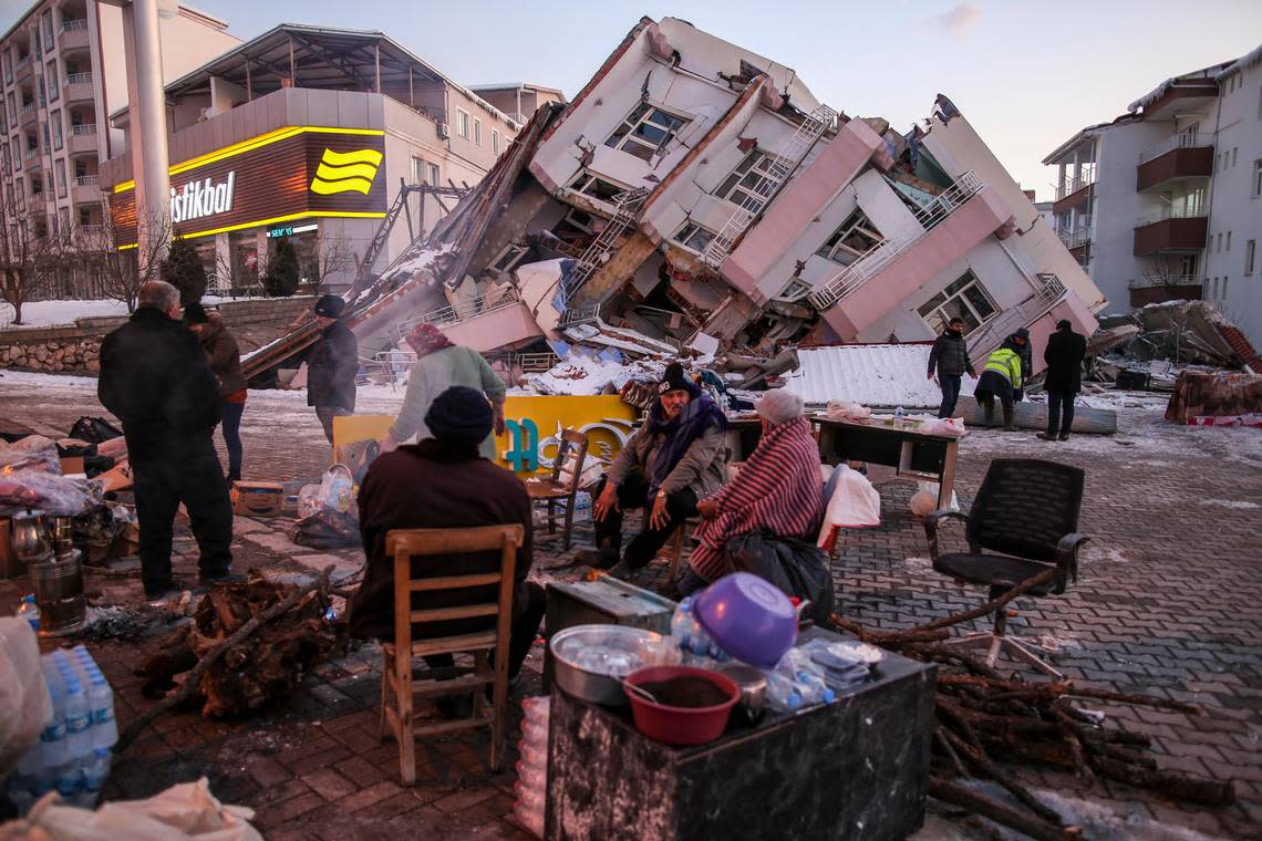 People sit and stand around a collapsed buildings in Golbasi, in Adiyaman province, southern Turkey, Wednesday, Feb. 8, 2023. Thinly stretched rescue teams worked through the night in Turkey and Syria, pulling more bodies from the rubble of thousands of buildings toppled by a catastrophic earthquake. The death toll rose Wednesday to more than 10,000, making the quake the deadliest in more than a decade. (AP Photo/Emrah Gurel)