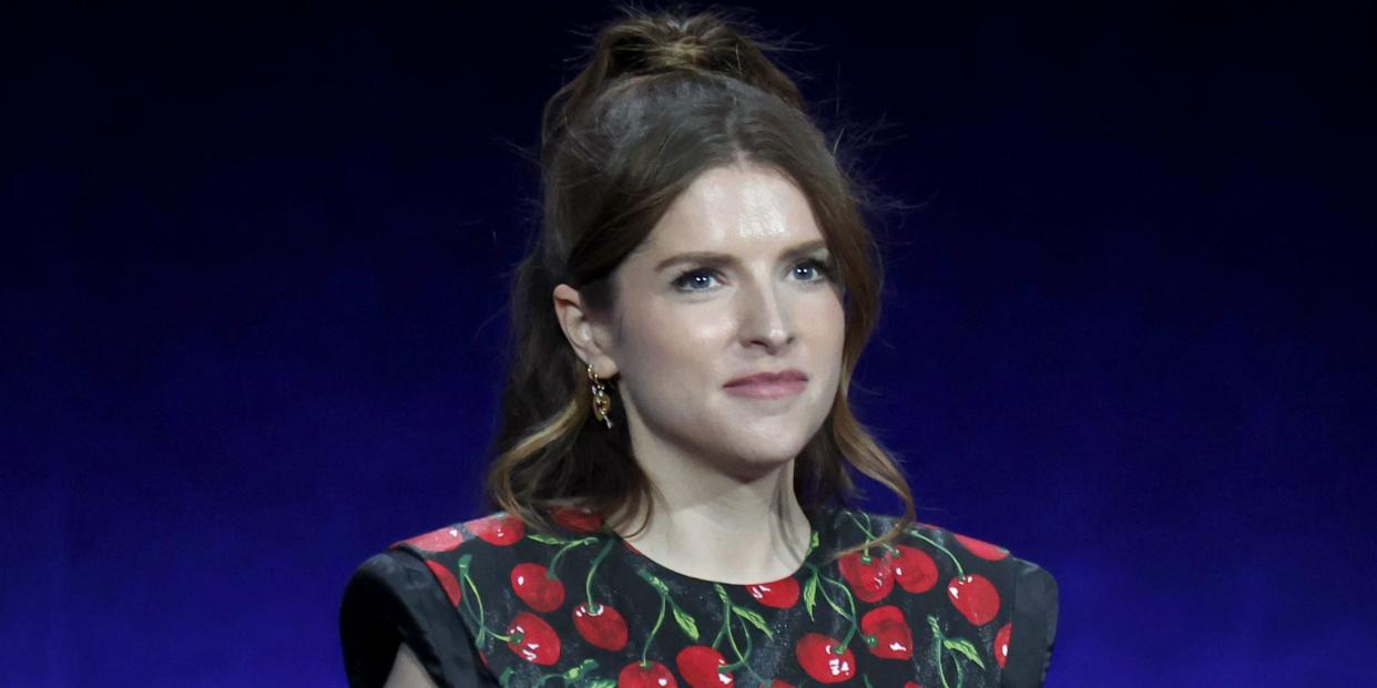 anna kendrick in a black dress with vine tomatoes, holding a microphone behind her back