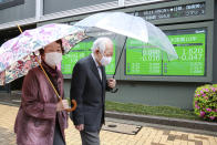 A couple wearing face masks walks by an electronic stock board of a securities firm in Tokyo, Wednesday, April 14, 2021. Asian stock markets rose Wednesday after Wall Street hit a high following an uptick in U.S. inflation and an order by regulators to suspend use of Johnson & Johnson's coronavirus vaccine. (AP Photo/Koji Sasahara)