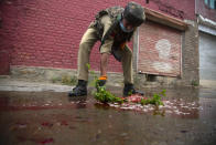 An Indian policeman cleans blood splattered on a street with a tree twig after suspected rebels attack on policemen on the outskirts of Srinagar, Indian controlled Kashmir, Friday, Aug. 14, 2020. Anti-India rebels in Indian-controlled Kashmir Friday attacked a police party in the disputed region's main city, killing two police officials and injuring another, police said. (AP Photo/Mukhtar Khan)