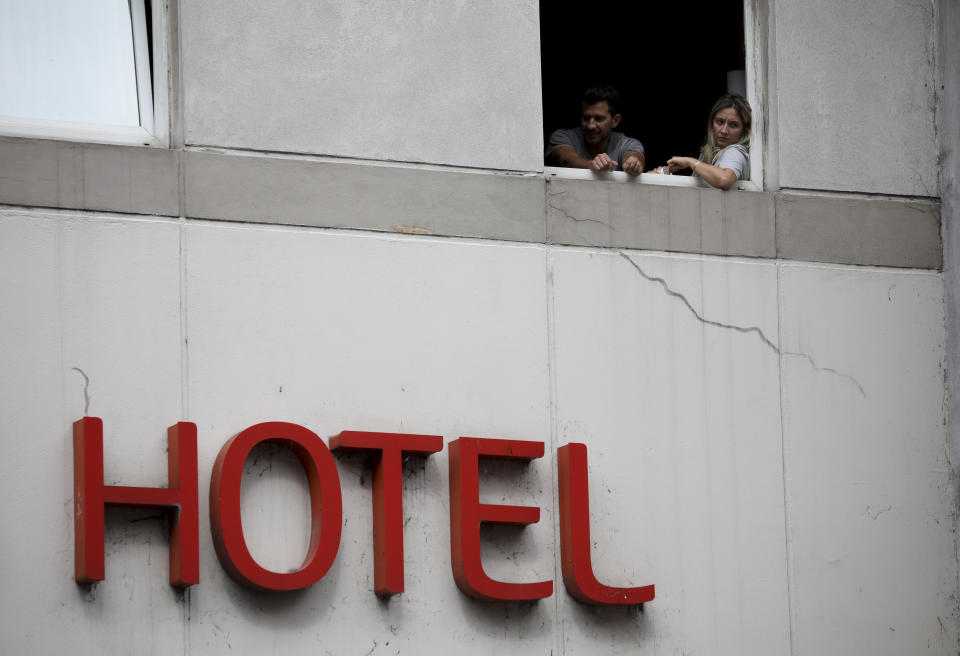 Una pareja que estuvo en el extranjero se asoma a través de la ventana de un hotel mientras está en cuarentena impuesta por el gobierno en Buenos Aires, Argentina, el miércoles 1 de abril de 2020. (AP Foto/Natacha Pisarenko)