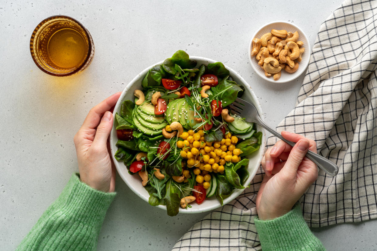 Anonymous female dining healthy vegan plant-based fibre salad in bowl with avocado, cashew, micro-greens, pok choi, chickpeas, tomato, lettuce, cucumber, sesame. Flexitarian fatty acids and dietary fiber