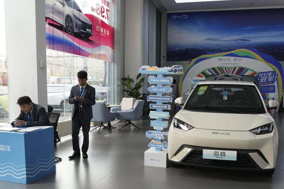 Sales staff stand near the Seagull electric vehicle from Chinese automaker BYD at a showroom in Beijing, Wednesday, April 10, 2024. The tiny, low-priced electric vehicle called the Seagull has American automakers and politicians trembling. The car, launched last year by Chinese automaker BYD, sells for around $12,000 in China. But it drives well and is put together with craftsmanship that rivals U.S.-made electric vehicles that cost three times as much. Tariffs on imported Chinese vehicles probably will keep the Seagull away from America’s shores for now.(AP Photo/Ng Han Guan)