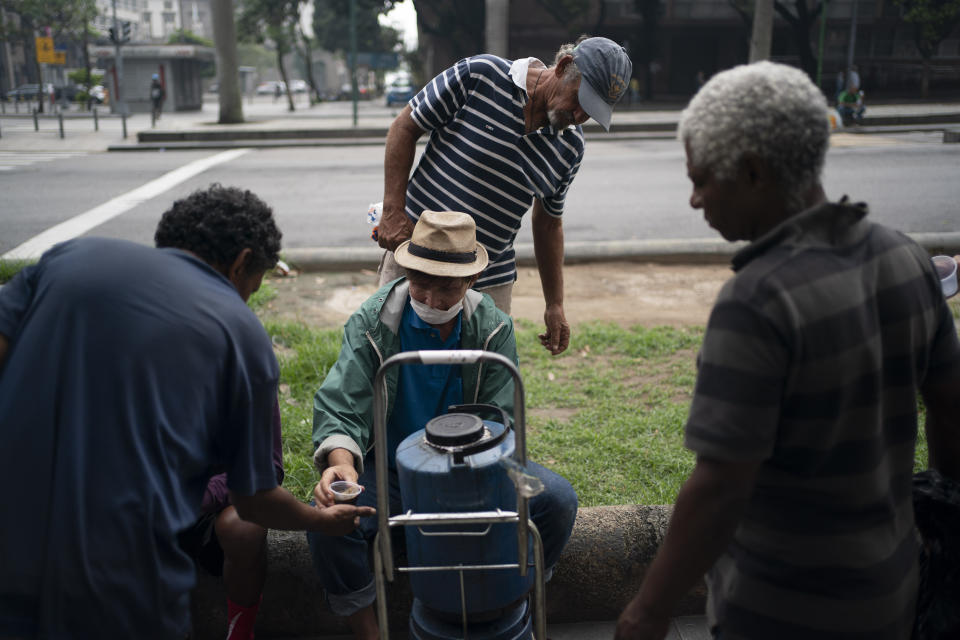 Homeless gather for a free cup of coffee and bread, distributed by Eli Ferreira, center, who started serving free breakfasts to the hungry daily since the outbreak of the new coronavirus, in downtown in Rio de Janeiro, Brazil, Monday, March 30, 2020. Ferreira, who used to serve food twice a week before the outbreak, said he knows he is breaking the rules of social distancing but that "what counts now is the human side." (AP Photo/Leo Correa)