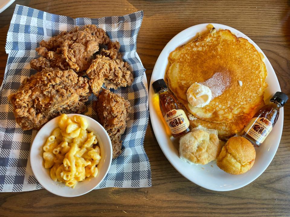 Basket of fried chicken and mac and cheese and a plate with two pancakes, containers of maple syrup, and cornbread and a biscuit