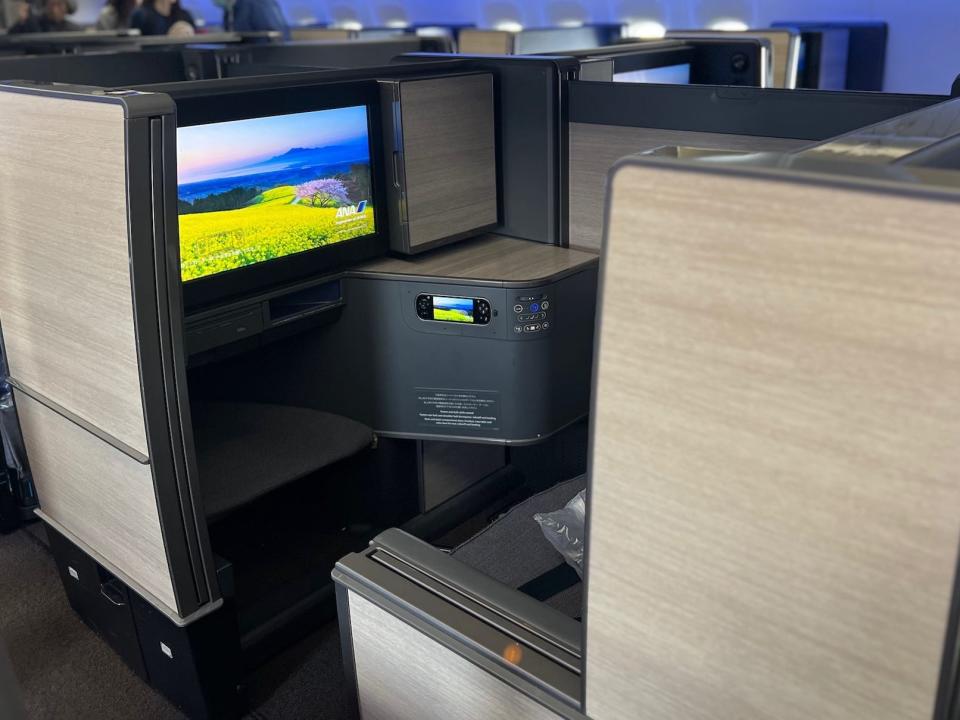 An open "The Room" business class seat with TV in view.