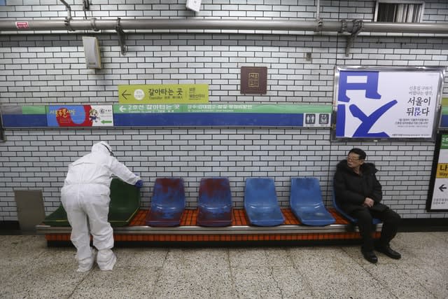 A worker wearing protective gear disinfects chairs as a precaution against the coronavirus at a subway station in Seoul, South Korea