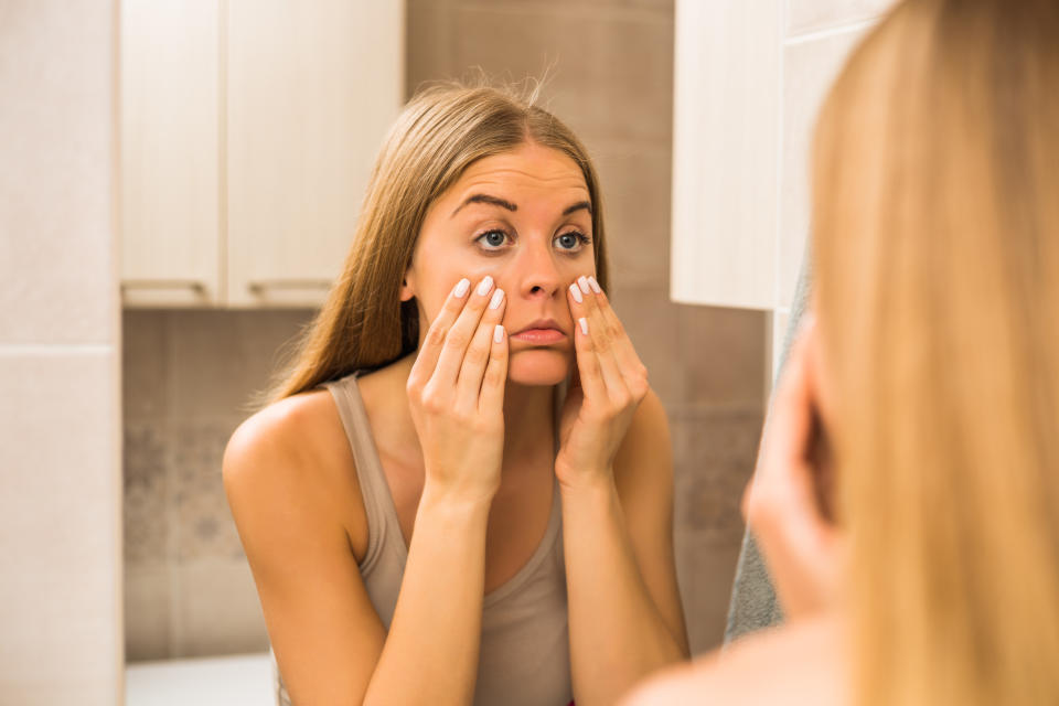 Tired woman looking her eye bags in the bathroom.