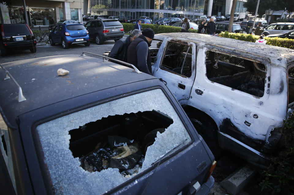 People look at a burned and damaged cars that was set on fire early Tuesday by supporters of the Shiite Hezbollah and Amal Movement groups, in Beirut, Lebanon, Tuesday, Dec. 17, 2019. Supporters of Lebanon's two main Shiite groups Hezbollah and Amal clashed with security forces and set fires to cars in the capital early Tuesday, apparently angered by a video circulating online that showed a man insulting Shiite figures.(AP Photo/Hussein Malla)