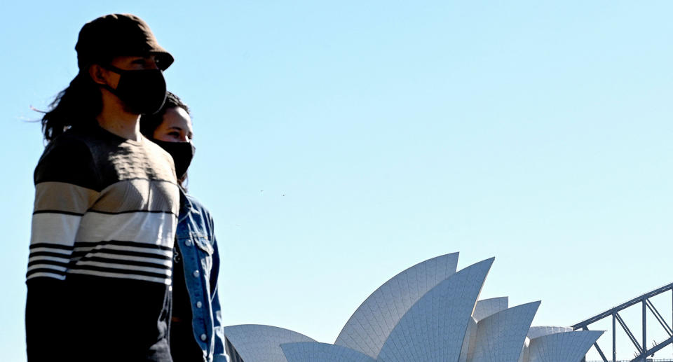 Two women walk past Sydney's Opera House wearing masks.