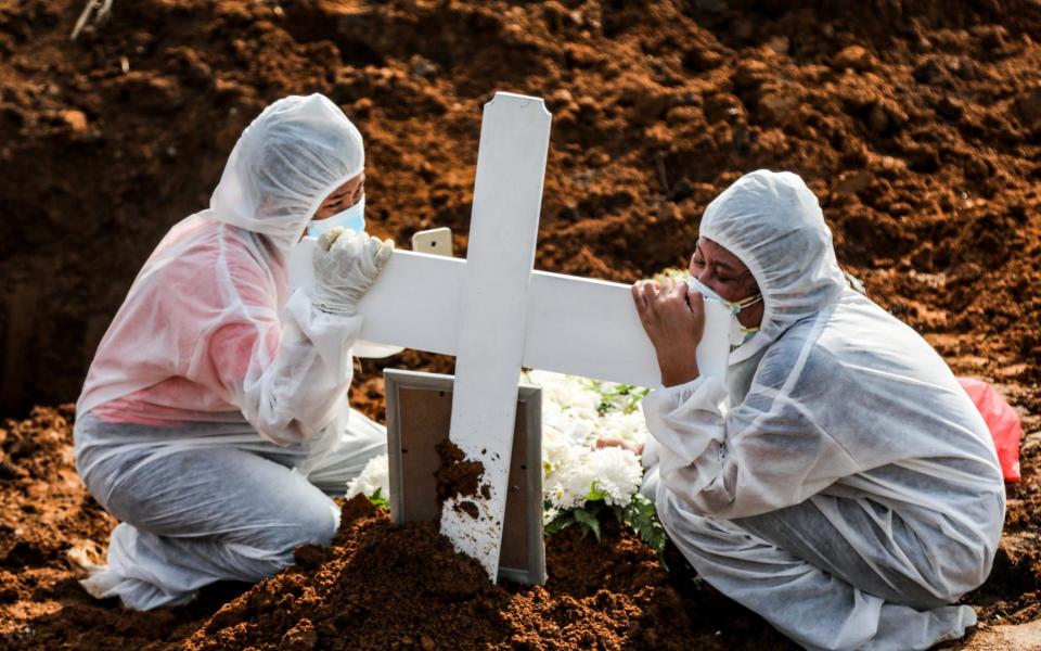 Relatives clad in hazmat suits mourn at the grave of a Covid-19 victim in Medan, Indonesia on 13 August 2021 - Dedi Sinuhaji/Shutterstock