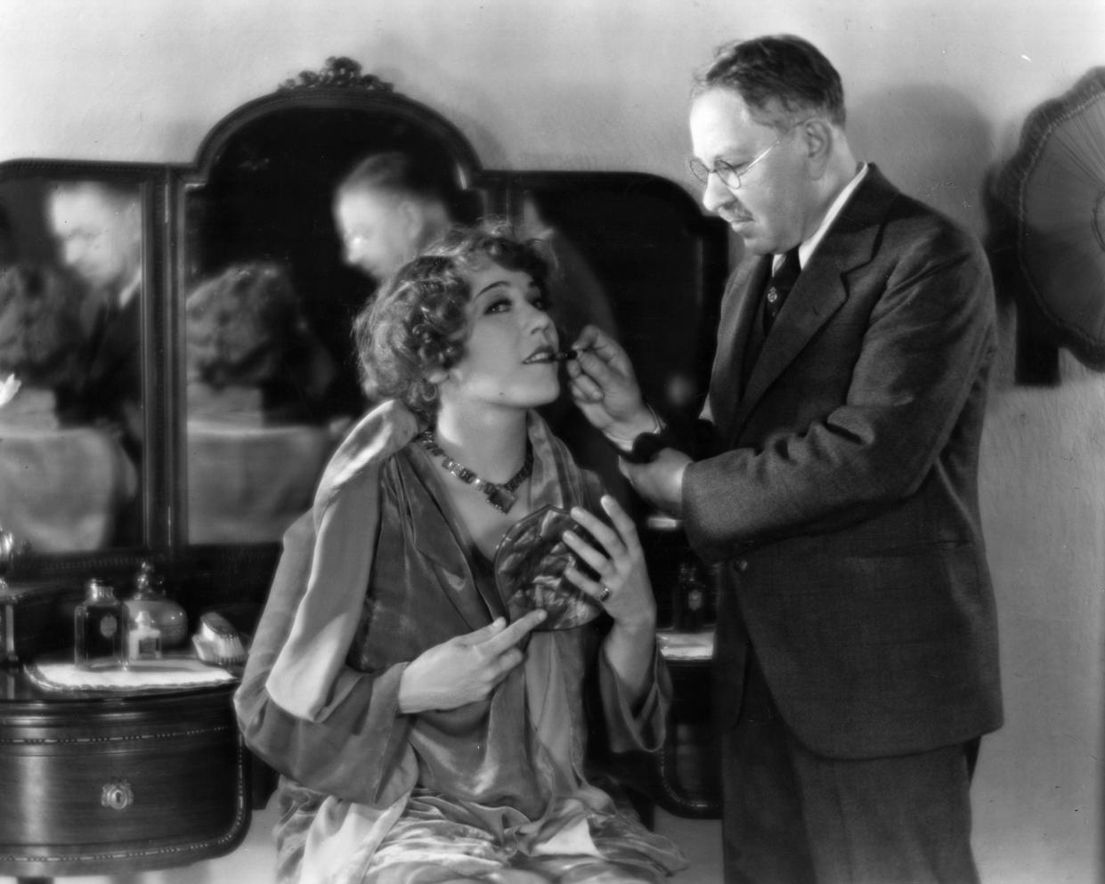 Louise Fazenda (1895 - 1962), the Hollywood film star and actress, is shown by 'the' Max Factor (1904 - 1996) how to apply lipstick