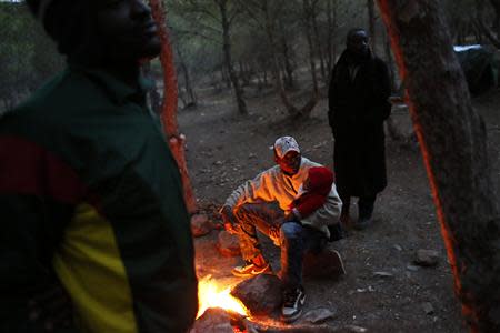 An African migrant warms himself by a fire at a clandestine campsite named Bolingo in northern Morocco near the border fence with Spain's north African enclave Melilla, November 28, 2013. REUTERS/Juan Medina