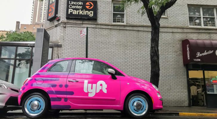 The Lyft (LYFT) logo on the side of a pink car parked on a street.