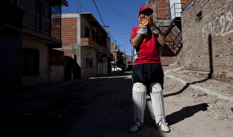 Caacupe cricket team member Alejandro Mercado covers his face with his gloved hands during a training session at the Villa 21-24 slum in Buenos Aires, Argentina, Saturday, March 22, 2014. The International Cricket Council has recognized the team, formed from the children of the Villa 21-24 shantytown, honoring them as a global example for expanding the sport, which in certain countries, like India, is widely played, but in many parts of the world restricted to elite sectors of society. Introducing cricket in the slum began in 2009 as an idea to transform the game into a social integration mechanism, before that it rarely breached the gates of the country's upscale private schools. (AP Photo/Natacha Pisarenko)