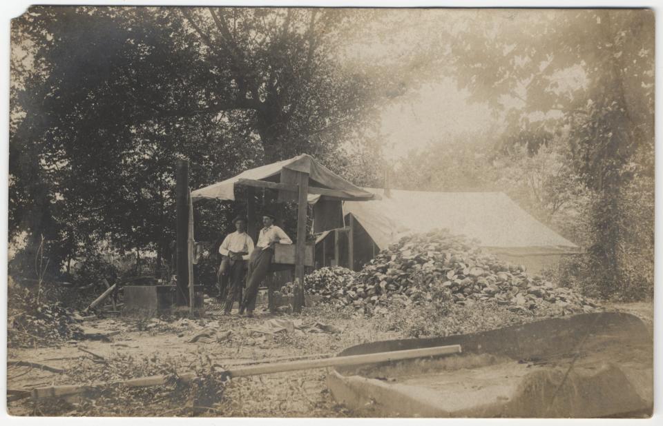 Two men taking a break from working on mussels in Indiana during the state's button boom. Freshwater mussels pulled out of creeks and rivers in the state were turned into mother-of-pearl buttons beginning in the early 1900s. This photo was digitized in 2009.