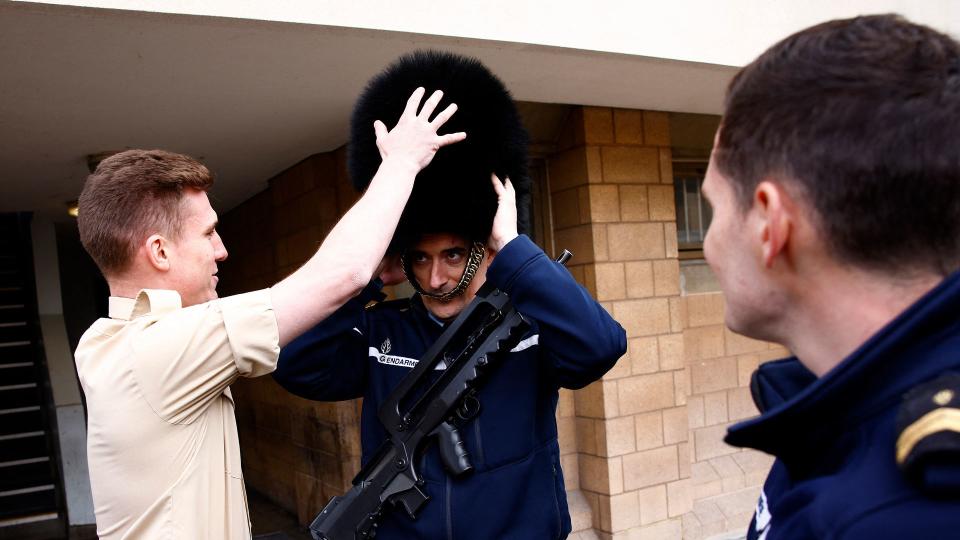 A member of France's Gendarmerie Garde Republicaine tries on the bearskin hat of a member of the British Army's F Company Scots Guards, following a rehearsal for a special Changing of the Guard ceremony, at Wellington Barracks 