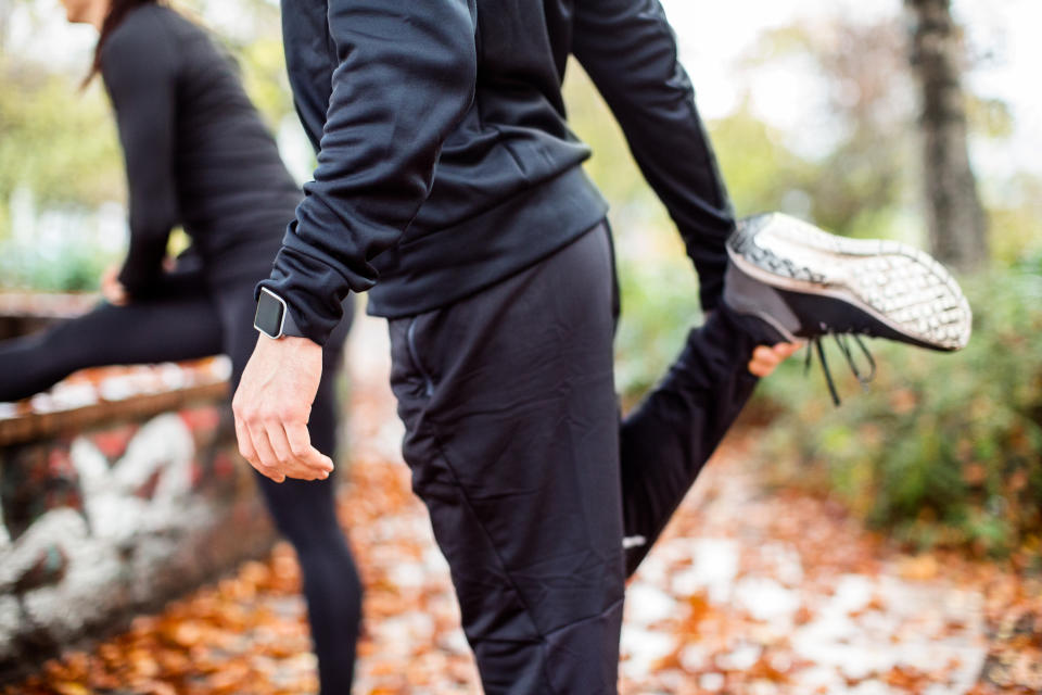 Mid section of young people stretching their legs at the park. Man in sports clothing and smartwatch doing warm ups before the run.