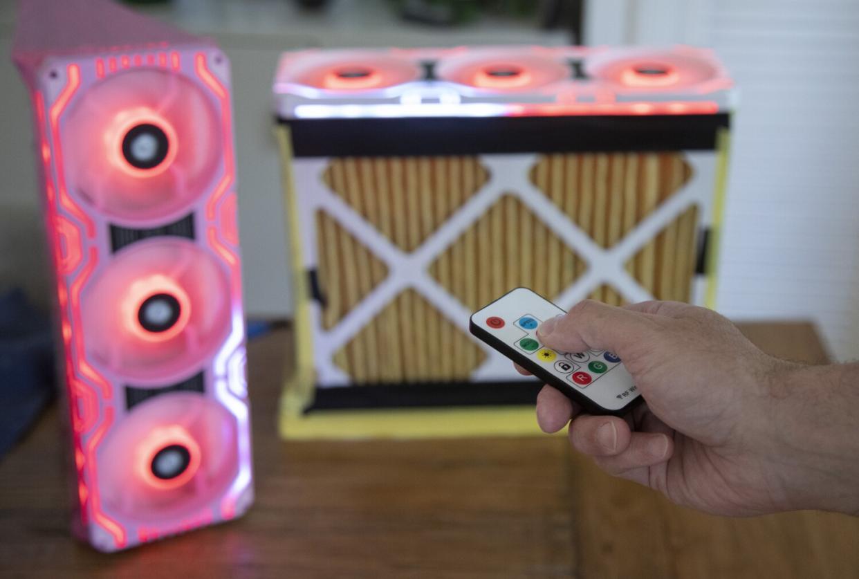 A hand with a remote control activates an air filter system made with computer fans.