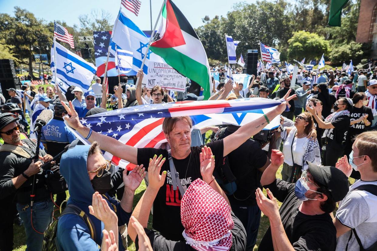 People hold U.S., Israeli and Palestinian flags in a crowd.