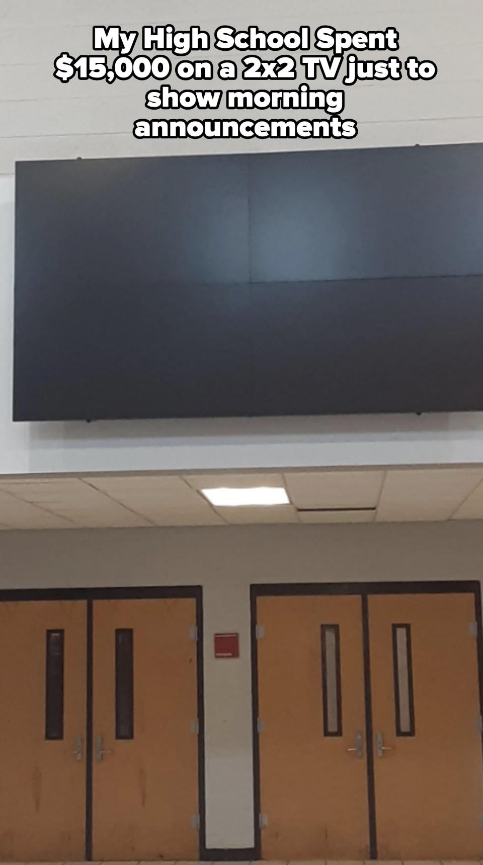 A large blank display screen mounted above a set of double doors in a public building