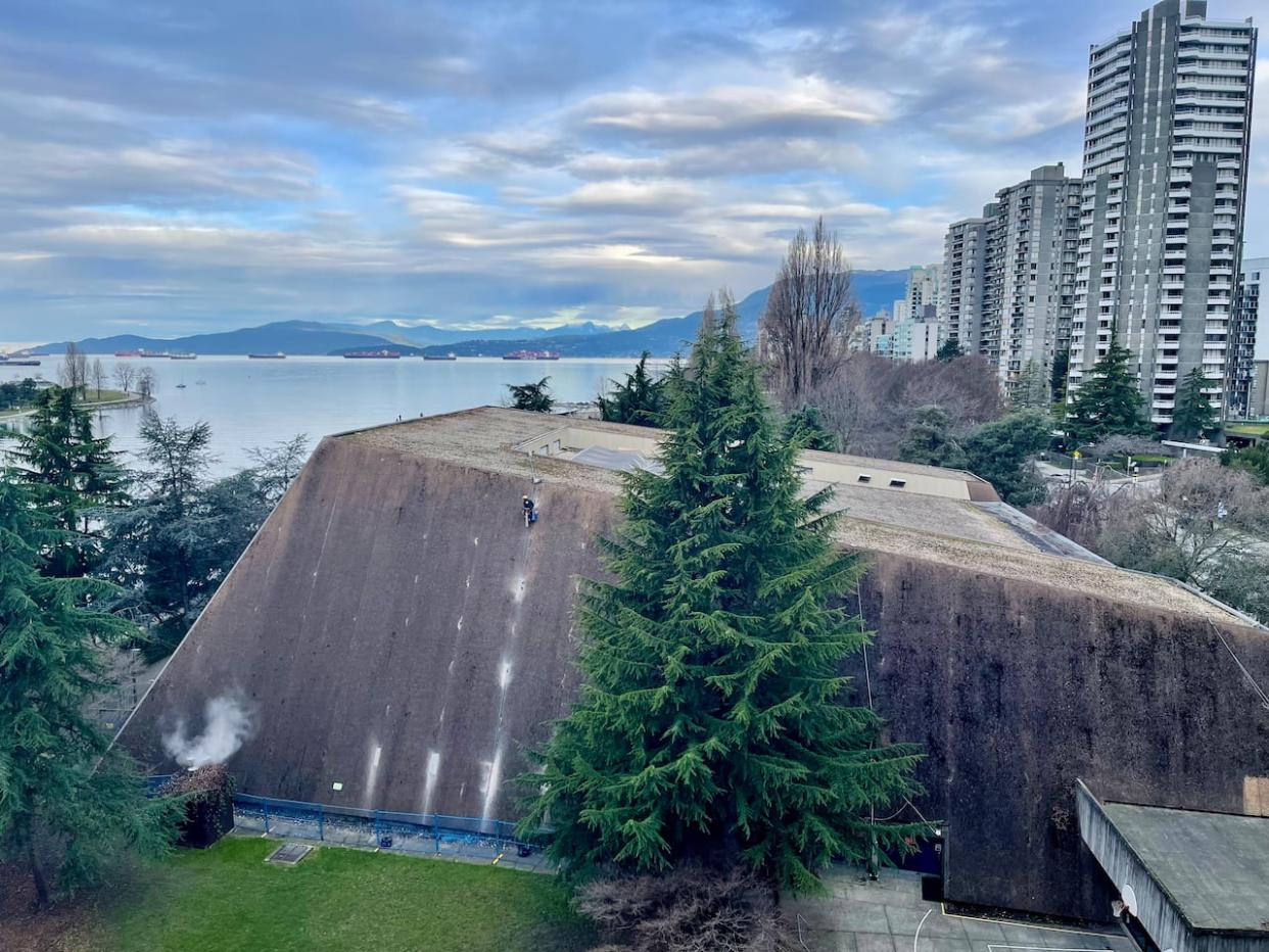 A worker rappels down the side of the Vancouver Aquatic Centre on Thursday. A piece of concrete fell from the ceiling, forcing the closure of two sections of the pool. (Karin Larsen/CBC - image credit)