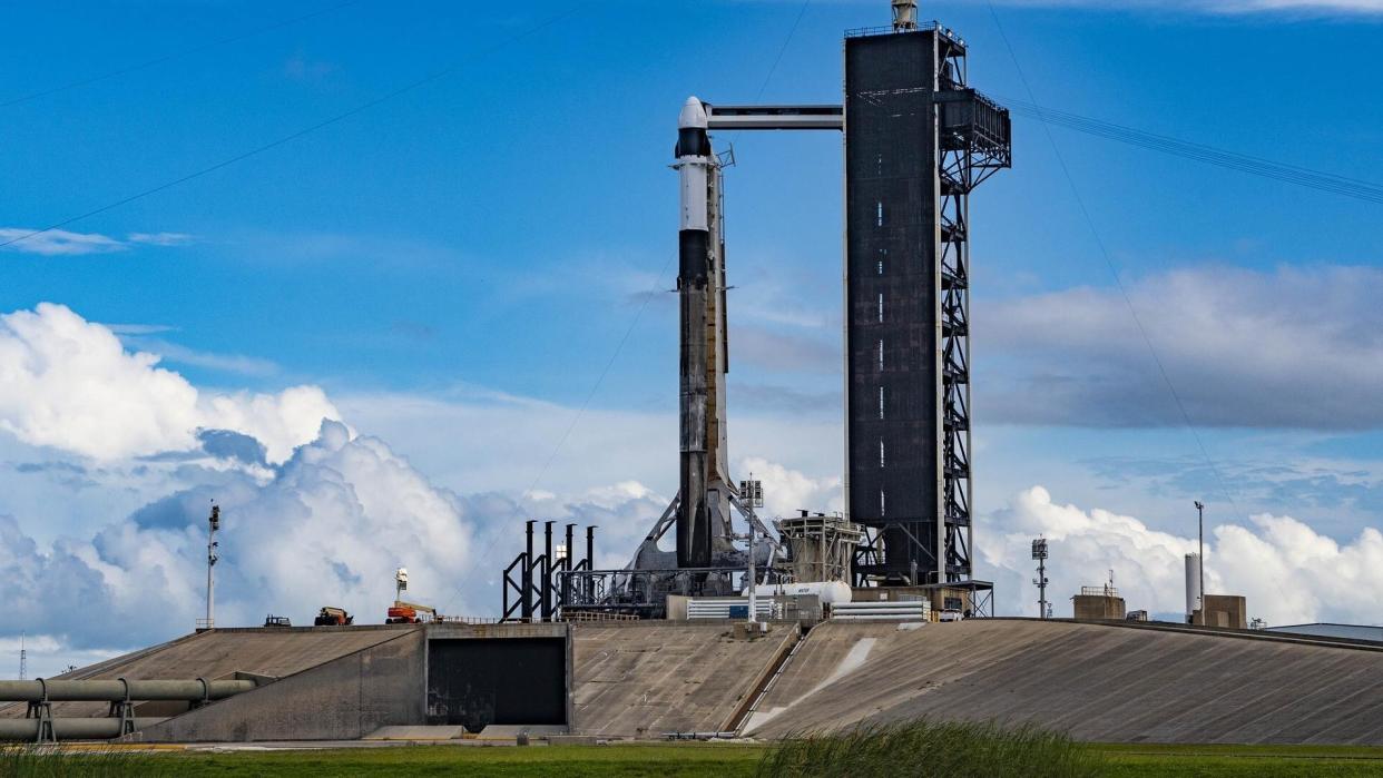  A rocket stands at a launchpad in front of a blue sky with majestic clouds. 