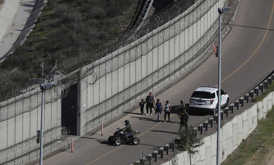 FILE - In this Dec. 16, 2018, file photo, Honduran asylum seekers are taken into custody by U.S. Border Patrol agents after the group crossed the U.S. border wall into San Diego, Calif., in this view from Tijuana, Mexico. Attorneys on Friday, Aug. 30, 2019, asked a judge to reject Trump administration plans to detain migrant families longer than they're allowed now and to remove court oversight of how children are treated in government custody. (AP Photo/Moises Castillo, File)
