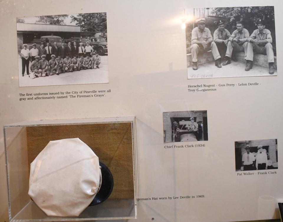 On the wall of the Old Town Hall Museum of Pineville are historical pictures of firemen whose unifiorms a placard notes were “affectionately named ‘The Fireman’s Grays.’ ” A fireman’s hat from 1969 belonging to Lee Deville is also in the display case, and a gray uniform hangs on a wall.