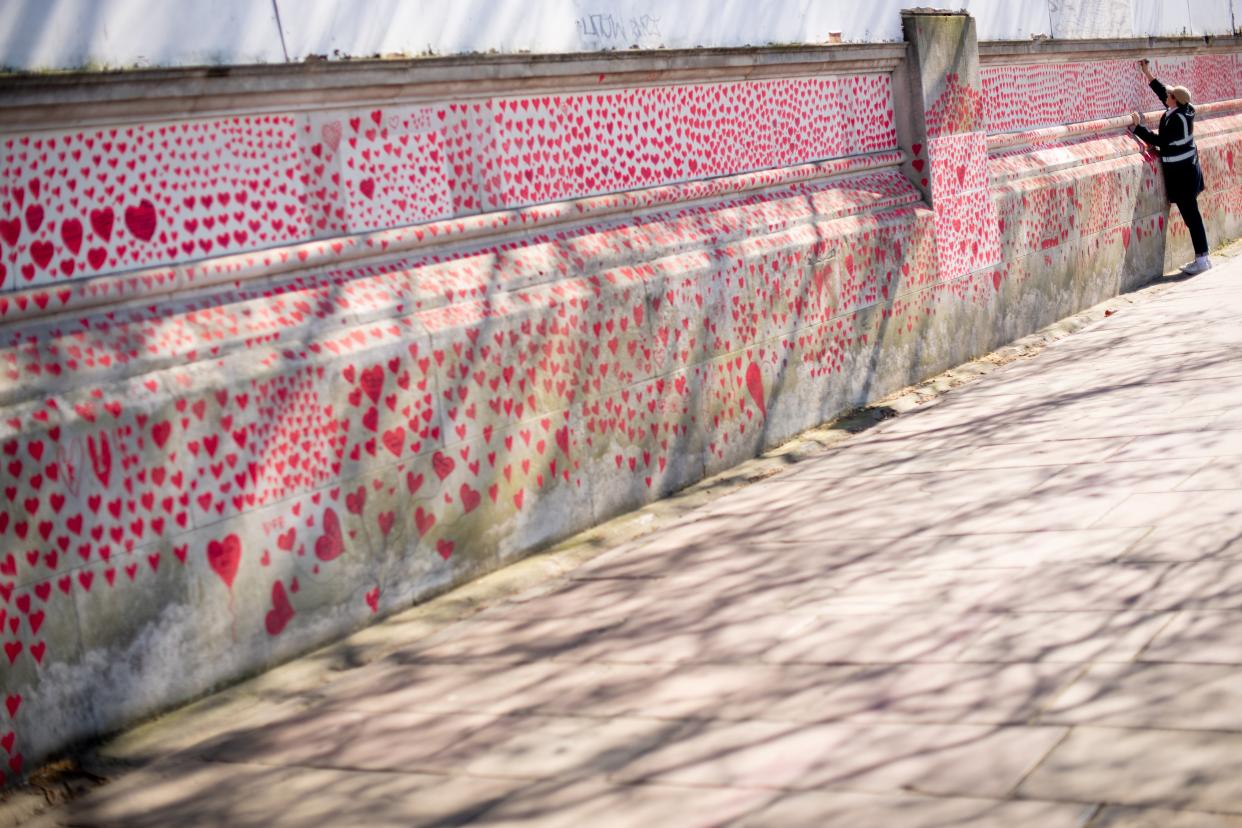 <p>A volunteer adds hearts to the Covid Memorial Wall in central London</p> (PA)