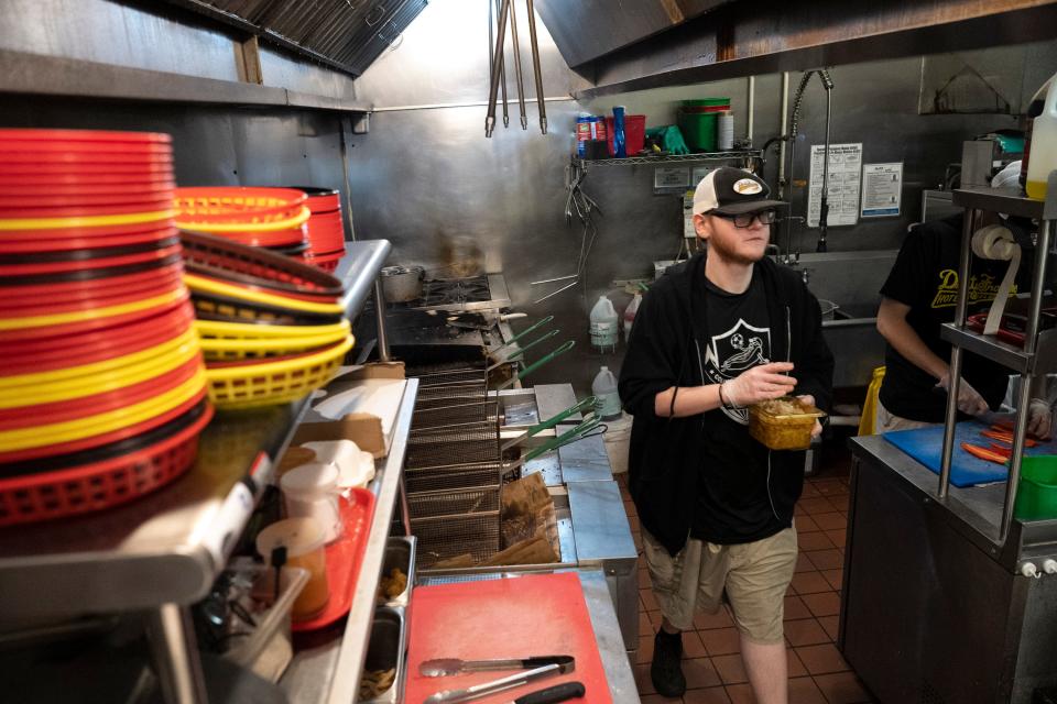 Jacob Buhrts carries fried onios through the kitchen during morning setup for the day at Dirty Frank’s Hot Dog Palace on Thursday Feb. 2, 2023.