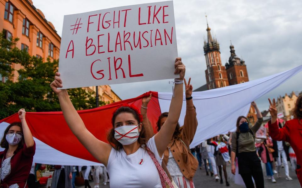 A demonstrator dressed in white wears a protective face mask and holds a banner during the a Women's march for Belarus in Poland