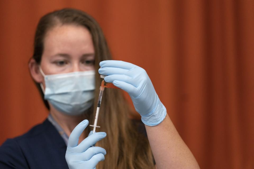 A woman in a face mask fills a syringe from a vial.