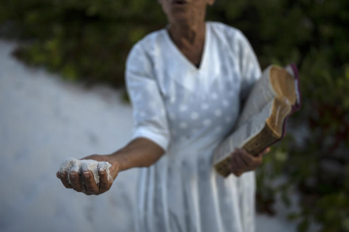 A woman holds a handful of sand as she prays in area of the Abaete dune system, that evangelicals have come to call the "Holy Mountain", in Salvador, Brazil, Tuesday, Sept. 13, 2022. Evangelicals have been converging on the dunes for some 25 years but especially lately, with thousands now coming each week to sing, pray and enter trancelike states to commune with God. (AP Photo/Rodrigo Abd)