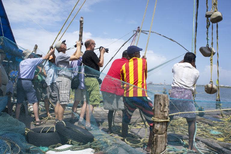 Tourists photograph Indian fishermen at work on Chinese fishing nets in Kochi, in southern Kerala, September 14, 2014