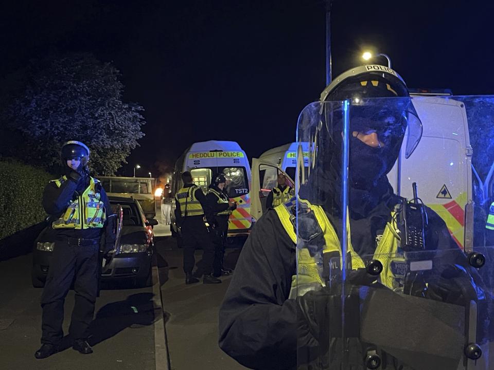 Police officers stand guard on Howell Road in Cardiff as they face a "large scale disorder" at the scene of a serious road traffic collision on Snowden Road in Ely, Cardiff, Tuesday, May 23, 2023. A few cars were set on fire and objects were hurled at police after a traffic accident Monday night in the Welsh capital Cardiff grew into what officials described as “large-scale disorder.”(Bronwen Weatherby/PA via AP)