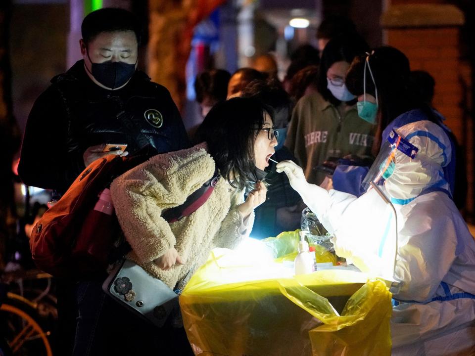 china covid worker in biohazard suit swabs womans mouth covid test with line of people waiting
