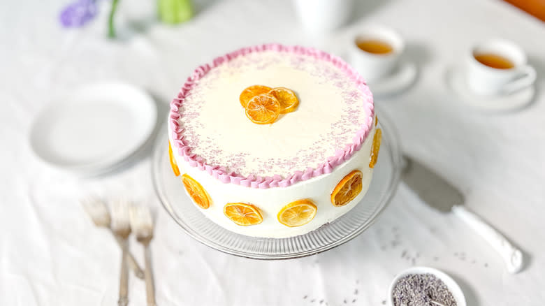 Bright and sunny lemon lavender cake on cake stand on table with serving wares and tea