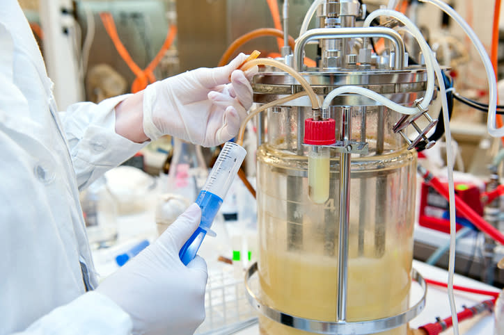 A lab-scale bioreactor being sampled by a scientist.