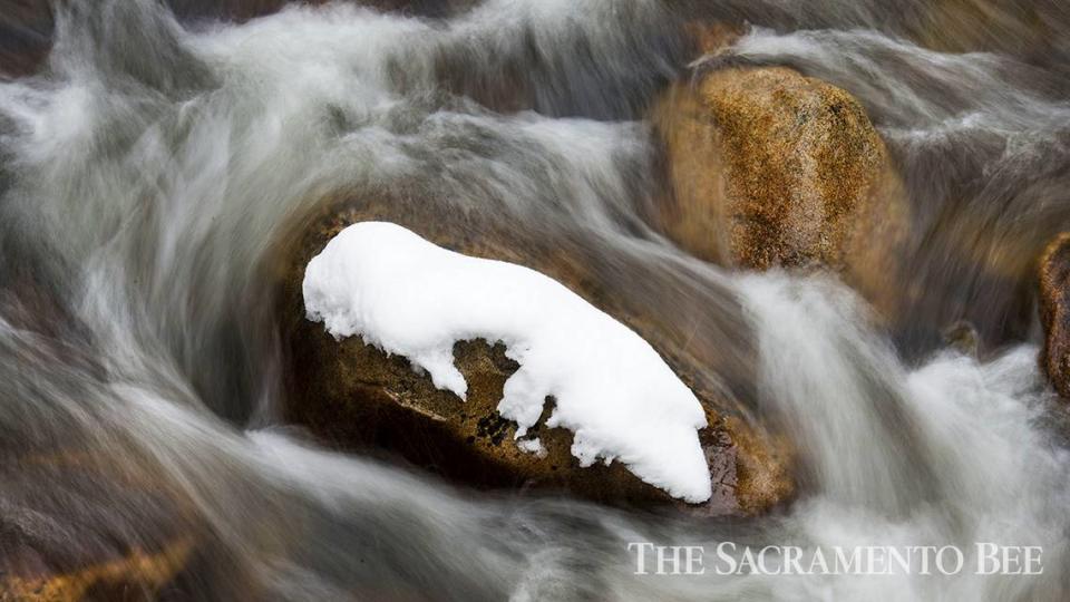 A snow-covered rock is surrounded by flowing water near the headwaters of the south fork of the American River in Strawberry.