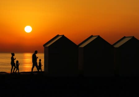 FILE PHOTO: A family walks beside beach cabins on a pebbled beach, during sunset as a heatwave hits France, in Cayeux-sur-Mer
