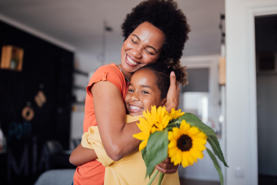 A woman and a young girl embracing, the girl holds a sunflower