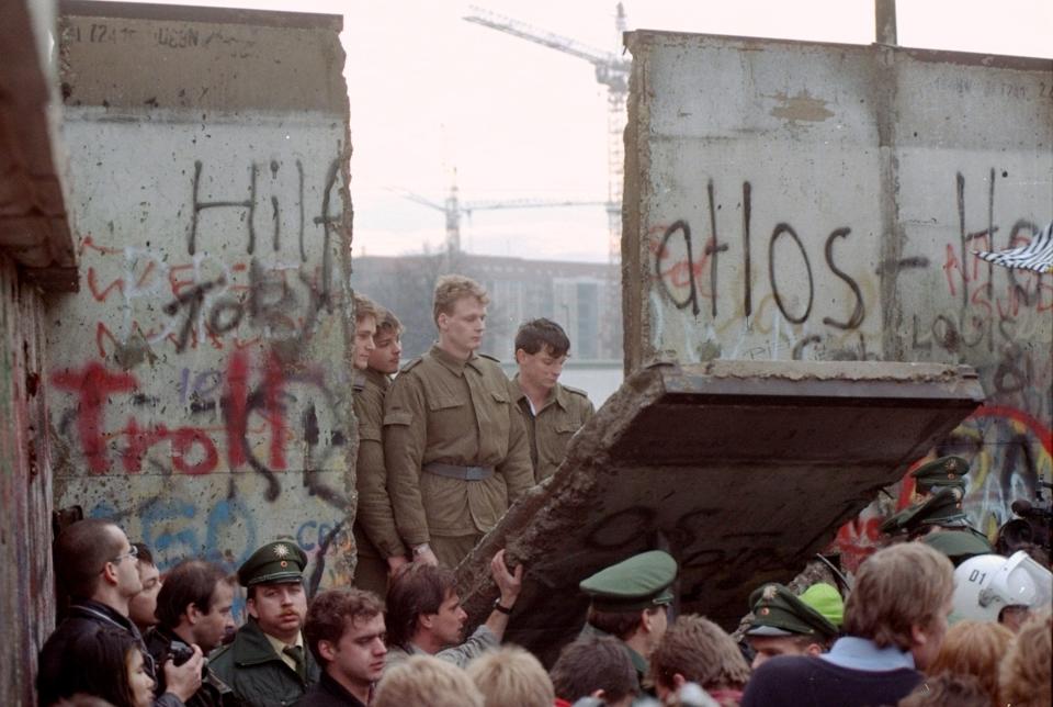 East German border guards look through a hole in the Berlin wall after demonstrators pulled down one segment of the wall at Brandenburg gate on Nov. 11, 1989.