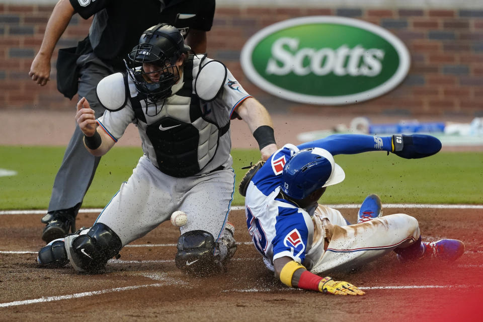 Atlanta Braves Ronald Acuna Jr., right, scores on a Marcell Ozuna base hit as the ball gets away from Miami Marlins catcher Chad Wallach, left, in the first inning of a baseball game Monday, April 12, 2021, in Atlanta. (AP Photo/John Bazemore)